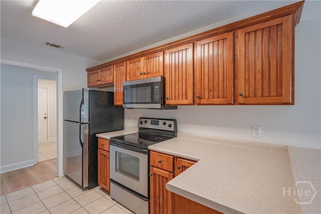 110 Pembroke Pl, Pembroke, GA 31321 - kitchen with appliances with stainless steel finishes, brown cabinets, light countertops, light tile patterned floors, and a textured ceiling