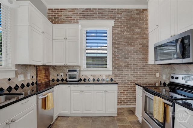 835 E Duffy St, Savannah, GA 31401 - kitchen featuring appliances with stainless steel finishes, brick wall, dark countertops, decorative backsplash, and white cabinets