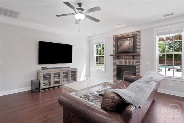 living room featuring dark wood-style floors, ornamental molding, baseboards, a brick fireplace, and a ceiling fan