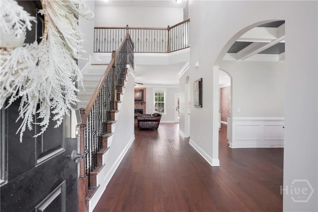 foyer entrance with hardwood / wood-style floors, stairway, arched walkways, a wainscoted wall, and baseboards