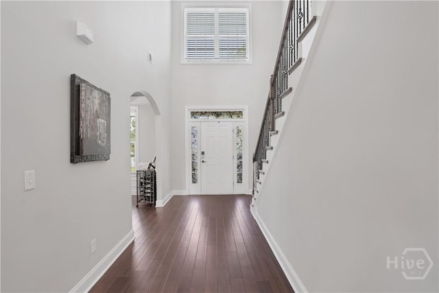 foyer entrance with arched walkways, baseboards, stairway, dark wood finished floors, and a high ceiling