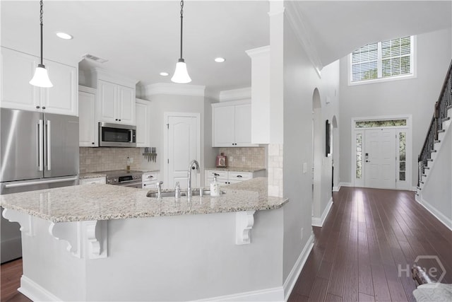 kitchen with appliances with stainless steel finishes, a sink, baseboards, a kitchen bar, and white cabinetry