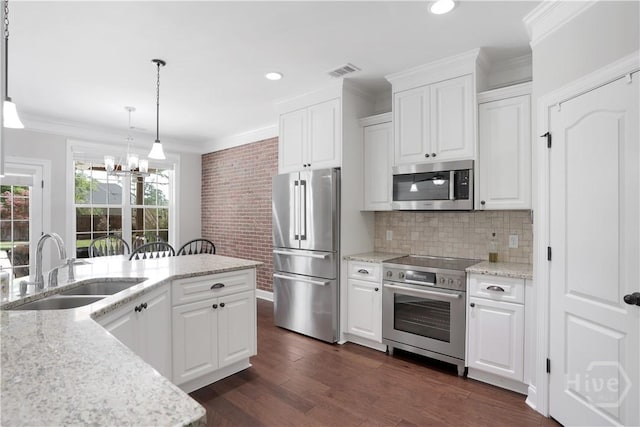 kitchen with appliances with stainless steel finishes, a sink, a chandelier, ornamental molding, and white cabinetry
