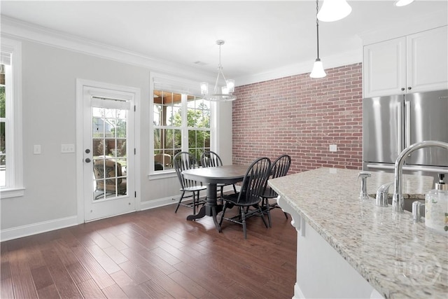 dining area featuring brick wall, crown molding, dark wood-style floors, a chandelier, and baseboards