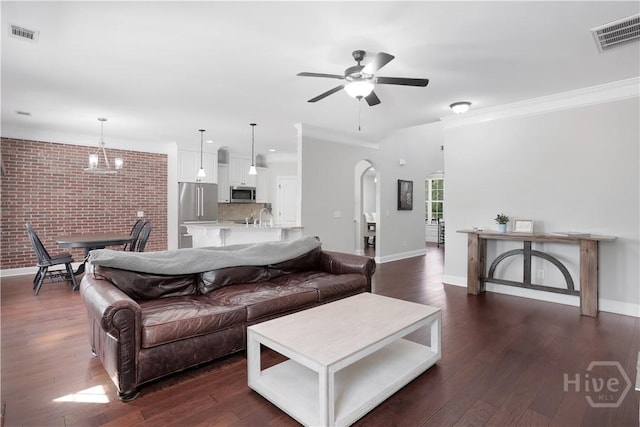 living area with arched walkways, a ceiling fan, dark wood-type flooring, baseboards, and ornamental molding