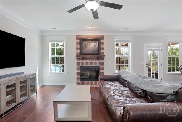living room with a fireplace, ornamental molding, dark wood-style floors, plenty of natural light, and ceiling fan