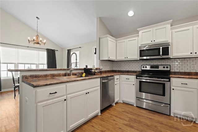 306 Madison Oaks Dr, Rincon, GA 31326 - kitchen featuring stainless steel appliances, a sink, dark countertops, vaulted ceiling, and a peninsula