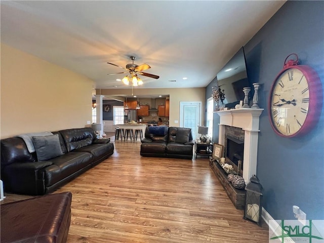 98 Vickers Rd SE, Ludowici, GA 31316 - living room featuring light wood-type flooring, a ceiling fan, a fireplace with raised hearth, and ornate columns