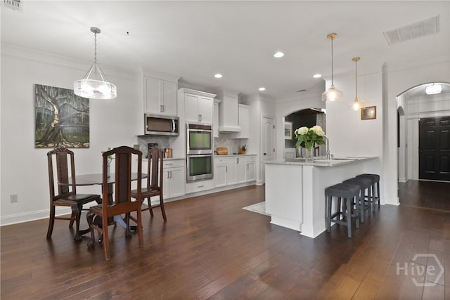 447 Walthour Dr, Rincon, GA 31326 - kitchen featuring stainless steel appliances, arched walkways, a kitchen bar, wall chimney range hood, and white cabinetry