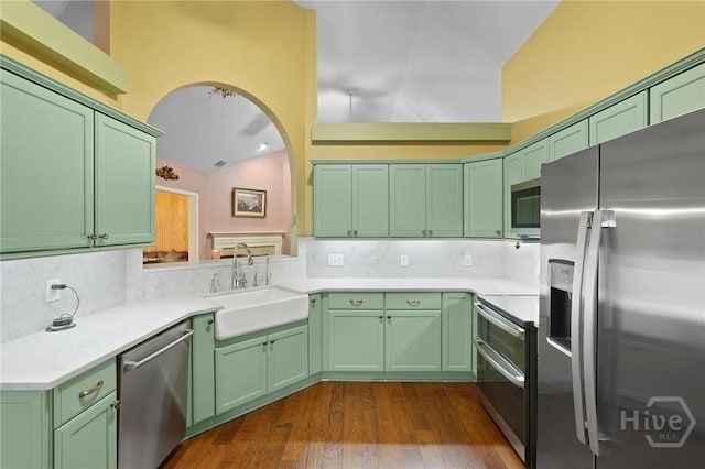kitchen with appliances with stainless steel finishes, a sink, green cabinets, dark wood-style flooring, and vaulted ceiling