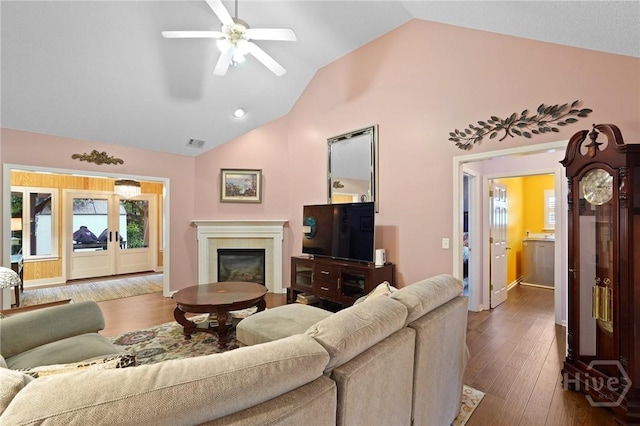 living area featuring lofted ceiling, a ceiling fan, a glass covered fireplace, wood finished floors, and baseboards