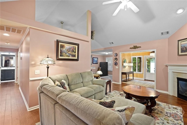 living room featuring a ceiling fan, baseboards, wood finished floors, vaulted ceiling, and a tiled fireplace