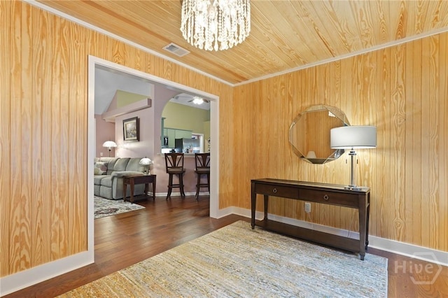 hallway with arched walkways, wood ceiling, wood walls, a chandelier, and baseboards
