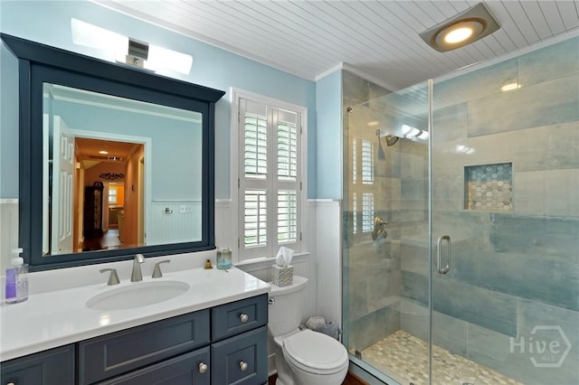 full bath featuring toilet, a shower stall, a wainscoted wall, vanity, and a decorative wall