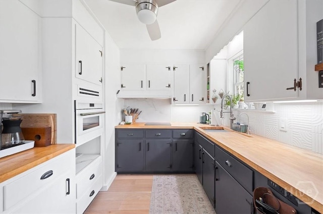 kitchen featuring oven, a ceiling fan, white cabinetry, light wood finished floors, and a sink