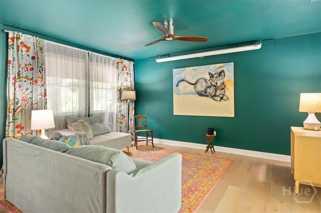living area featuring baseboards, wood finished floors, and a ceiling fan