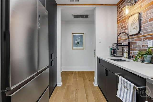 321 Abercorn St Unit 404, Savannah, GA 31401 - kitchen with freestanding refrigerator, dark cabinets, light wood finished floors, light countertops, and brick wall
