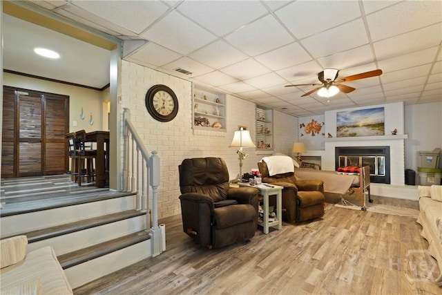 3010 Leonard St, Savannah, GA 31404 - living area featuring a fireplace, ceiling fan, wood finished floors, a paneled ceiling, and brick wall