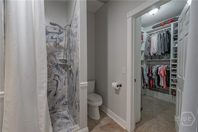 bathroom featuring toilet, a shower stall, a spacious closet, baseboards, and a textured ceiling