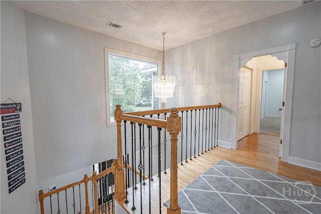 corridor featuring an upstairs landing, wood finished floors, a chandelier, a textured ceiling, and baseboards