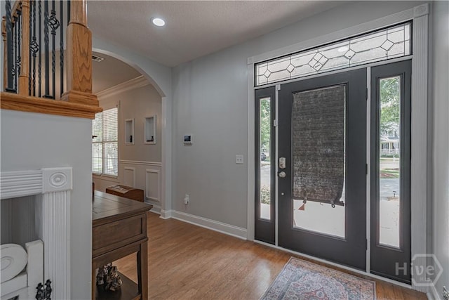 entryway with arched walkways, wood finished floors, recessed lighting, crown molding, and baseboards