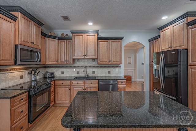 kitchen featuring black appliances, a sink, arched walkways, crown molding, and light wood-type flooring