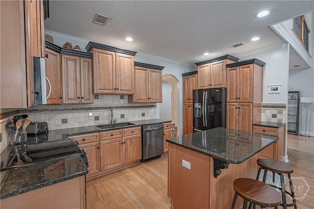 kitchen featuring stainless steel appliances, ornamental molding, arched walkways, a sink, and light wood-style flooring