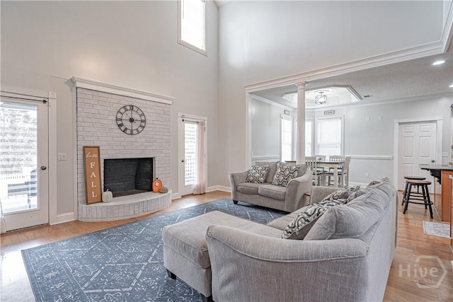 living room featuring healthy amount of natural light, wood finished floors, crown molding, a brick fireplace, and a towering ceiling