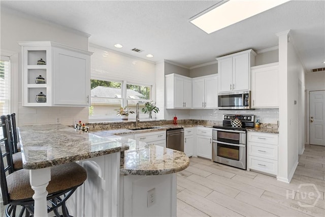 245 Montauk Dr, Richmond Hill, GA 31324 - kitchen featuring appliances with stainless steel finishes, a sink, a peninsula, white cabinetry, and ornamental molding