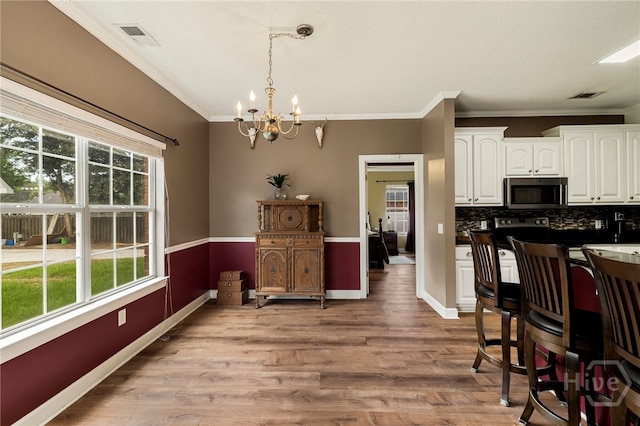 209 Saint James Walk, Guyton, GA 31312 - kitchen featuring stainless steel microwave, ornamental molding, a chandelier, white cabinetry, and light wood-type flooring
