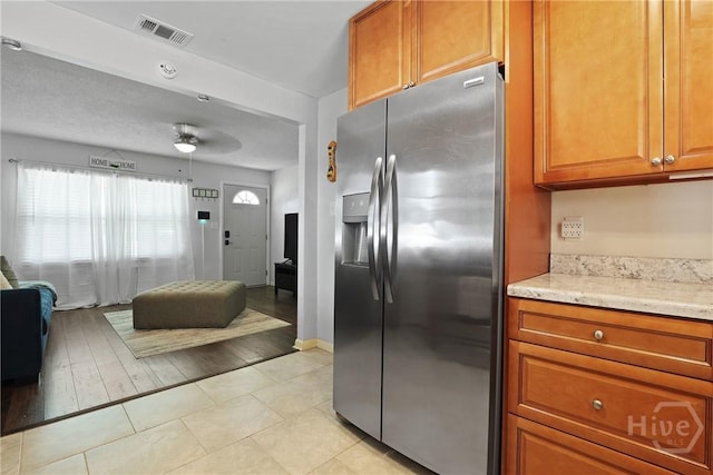 1504 Audubon Dr, Savannah, GA 31415 - kitchen with stainless steel refrigerator with ice dispenser, brown cabinetry, light tile patterned flooring, and light stone countertops