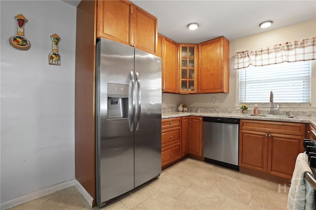 1504 Audubon Dr, Savannah, GA 31415 - kitchen with stainless steel appliances, a sink, brown cabinetry, glass insert cabinets, and light stone countertops