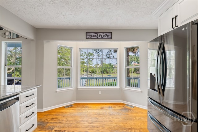 108 San Marco Dr, Tybee Island, GA 31328 - kitchen featuring appliances with stainless steel finishes, a textured ceiling, light stone counters, light wood-style flooring, and white cabinetry
