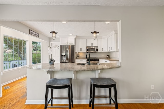 108 San Marco Dr, Tybee Island, GA 31328 - kitchen featuring appliances with stainless steel finishes, white cabinets, light stone counters, a peninsula, and pendant lighting