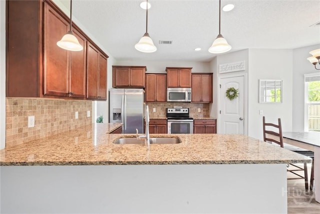 821 NE Mustang Ln, Ludowici, GA 31316 - kitchen with stainless steel appliances, a sink, a peninsula, brown cabinets, and light stone countertops
