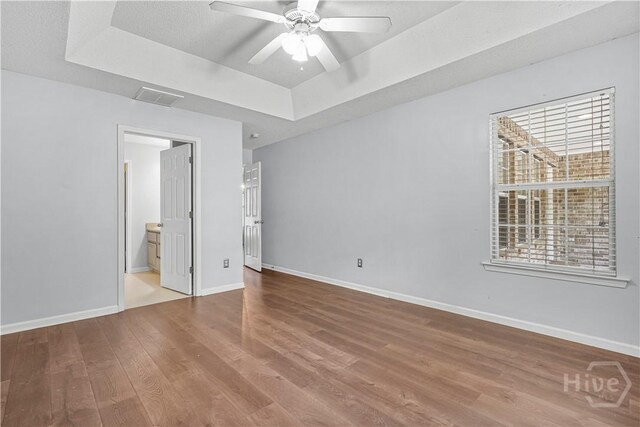 125 Crossing Cir, Rincon, GA 31326 - unfurnished bedroom featuring a tray ceiling, wood finished floors, baseboards, ensuite bathroom, and a ceiling fan