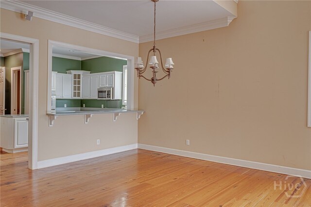 2 Franklin Creek Rd S, Savannah, GA 31411 - kitchen with stainless steel microwave, a kitchen breakfast bar, white cabinets, ornamental molding, and light wood-style floors