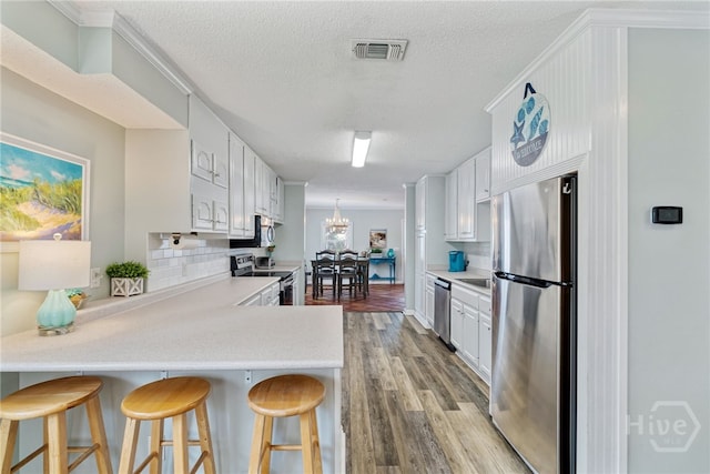1406 Jones Ave, Tybee Island, GA 31328 - kitchen featuring stainless steel appliances, a peninsula, light wood-type flooring, a textured ceiling, and white cabinetry