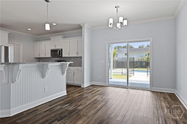 194 Shortleaf Trl, Richmond Hill, GA 31324 - kitchen with stainless steel microwave, dark wood-style floors, white cabinetry, a chandelier, and a breakfast bar area