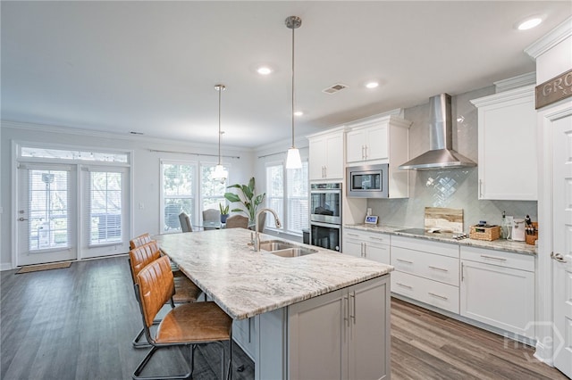 32 Brookhaven Dr, Savannah, GA 31407 - kitchen featuring wall chimney range hood, stainless steel appliances, wood finished floors, a breakfast bar, and a center island with sink