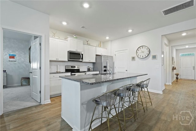 116 Fremont Ln, Pooler, GA 31322 - kitchen featuring stainless steel appliances, a kitchen island with sink, a kitchen breakfast bar, light wood-type flooring, and white cabinetry