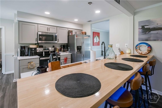 3 Black Forest Dr, Savannah, GA 31410 - kitchen featuring appliances with stainless steel finishes, gray cabinetry, dark wood finished floors, a kitchen breakfast bar, and ornamental molding