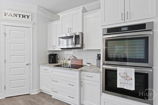 150 Pitch Point Trl, Richmond Hill, GA 31324 - kitchen featuring appliances with stainless steel finishes, white cabinetry, light stone countertops, decorative backsplash, and wood finished floors
