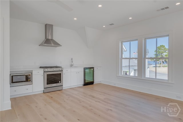 630 Ogeechee Ln, Richmond Hill, GA 31324 - kitchen featuring appliances with stainless steel finishes, wall chimney range hood, light wood-style floors, white cabinetry, and a sink