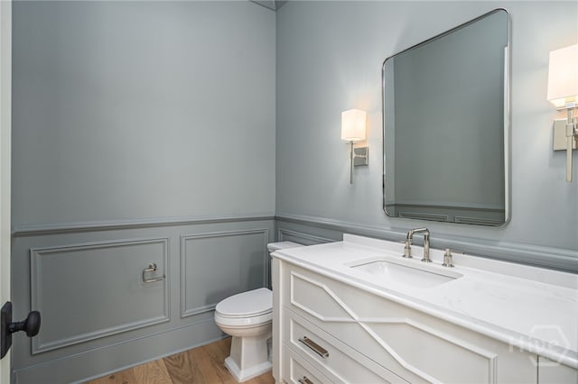 630 Ogeechee Ln, Richmond Hill, GA 31324 - half bath featuring toilet, vanity, a decorative wall, a wainscoted wall, and wood finished floors