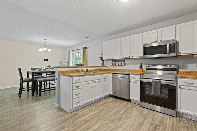 21 Hawser Way, Port Wentworth, GA 31407 - kitchen featuring appliances with stainless steel finishes, light wood-style flooring, a peninsula, white cabinetry, and a textured ceiling