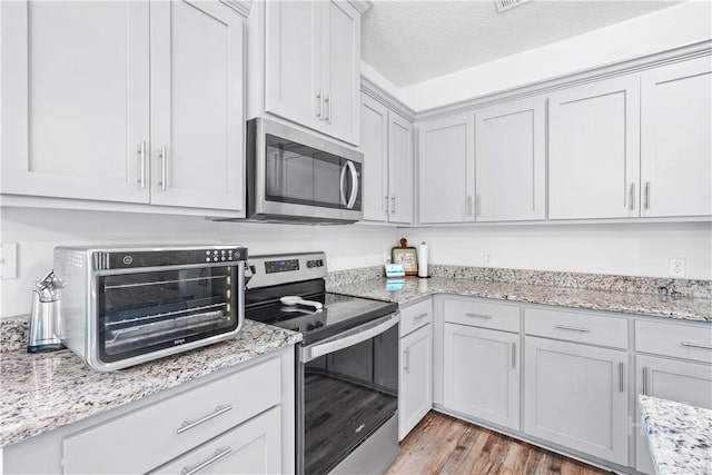 208 Cherokee Oaks Xing, Hinesville, GA 31313 - kitchen with appliances with stainless steel finishes, light wood finished floors, light stone counters, and a textured ceiling