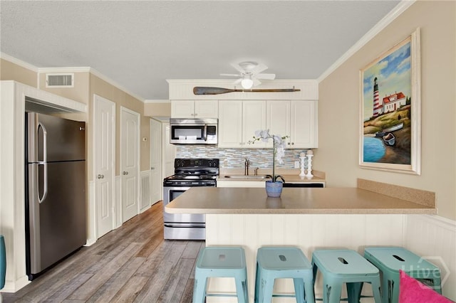 1217 Bay St Unit 105B, Tybee Island, GA 31328 - kitchen with stainless steel appliances, light wood-style flooring, a peninsula, decorative backsplash, and ornamental molding