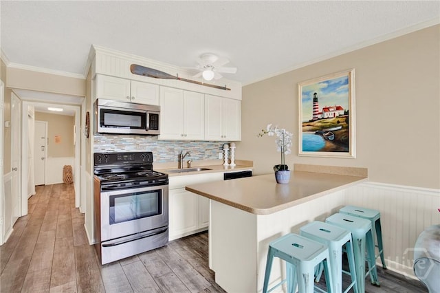 1217 Bay St Unit 105B, Tybee Island, GA 31328 - kitchen with appliances with stainless steel finishes, ornamental molding, light countertops, white cabinets, and a wainscoted wall
