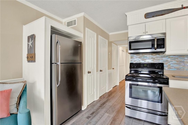 1217 Bay St Unit 105B, Tybee Island, GA 31328 - kitchen featuring stainless steel appliances, white cabinets, light wood-style flooring, light countertops, and decorative backsplash